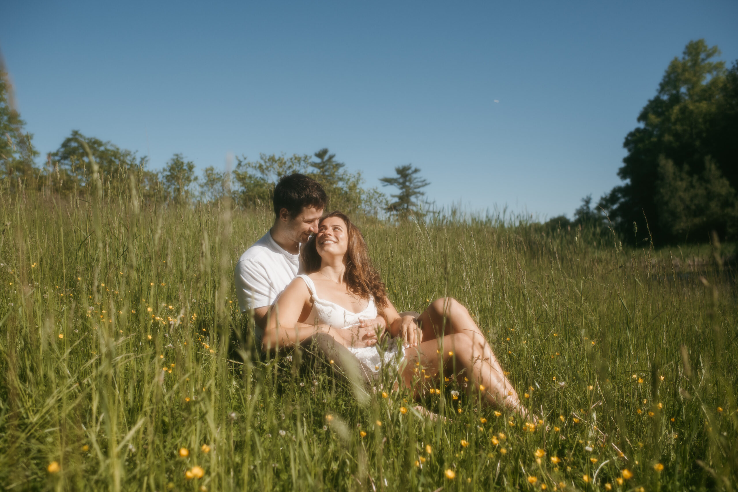 Couple sitting in a meadow at Waywayanda Lake in NJ by Sydney Madison Creative